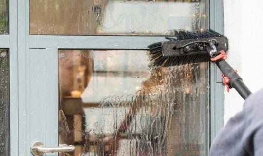 Water-fed brush cleaning a glass door